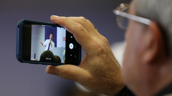 Someone with gray hair and glasses records Pete Buttigieg on his phone.