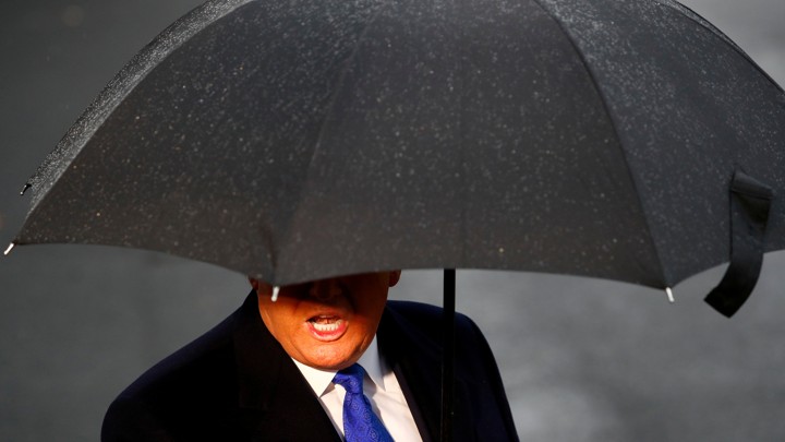 President Donald Trump's face is slightly obscured by a large black umbrella.