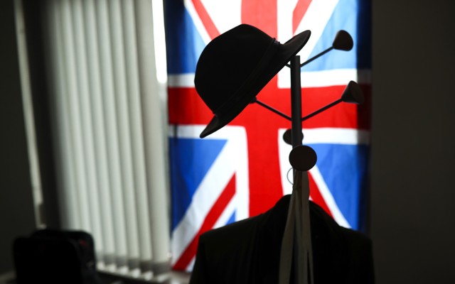 An image of a hat hanging on a hook in front of the Union Jack flag.