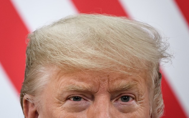 Top half of President Donald Trump's head in front of red and white stripes of the American flag
