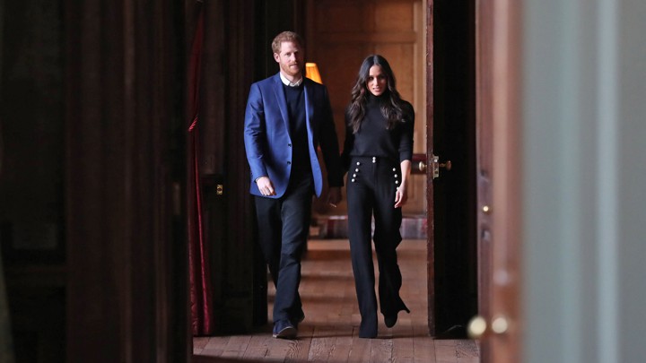 Prince Harry and Meghan Markle walk down a hallway.