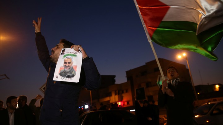 A man holds a photo of Qassem Soleimani, surrounded by others on a dark street in Tehran, celebrating after Iran launched missiles at U.S. forces in Iraq.