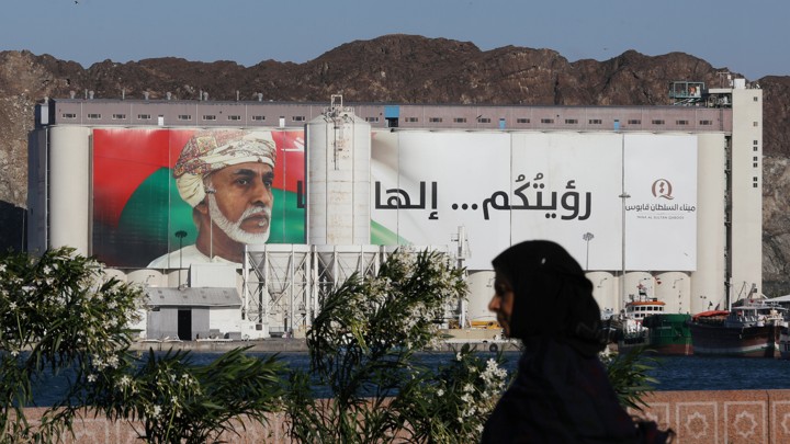 A woman walking past portrait of Sultan Qaboos