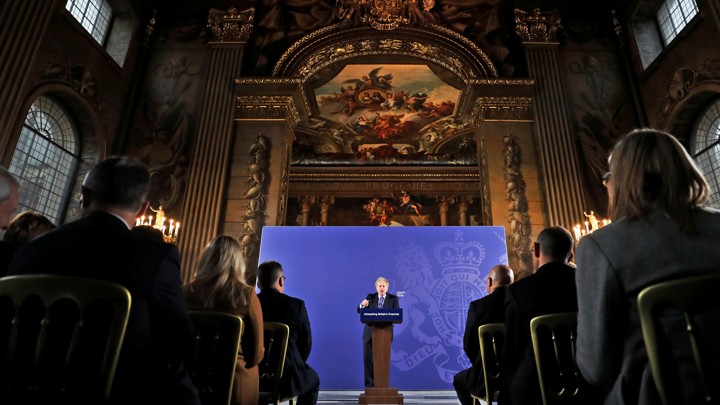 British Prime Minister Boris Johnson gives a speech at the front of an ornate room.