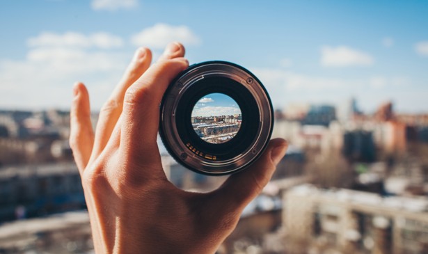 A view of a city through a camera lens held up by a hand