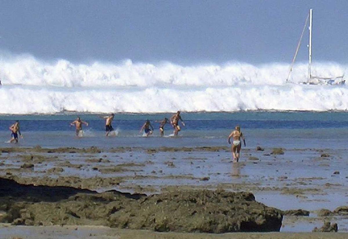 Foreign tourists far out on the sand after the water receded react as the first of six tsunami waves started to roll towards Hat Rai Lay Beach, near Krabi in southern Thailand,