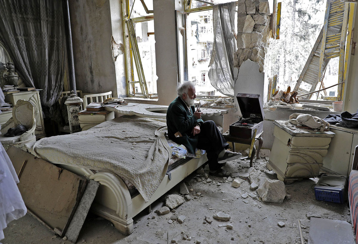 Abu Omar, smokes his pipe as he sits in his destroyed bedroom. Photo by Joseph Eid.