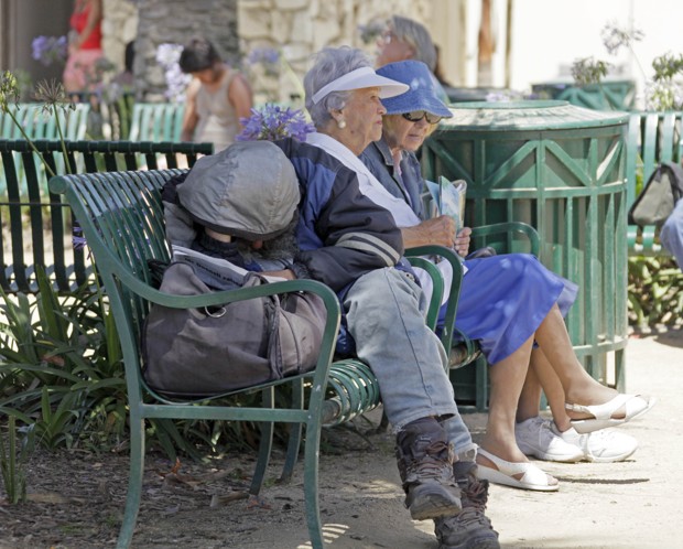 A homeless man and two elderly women share a bench