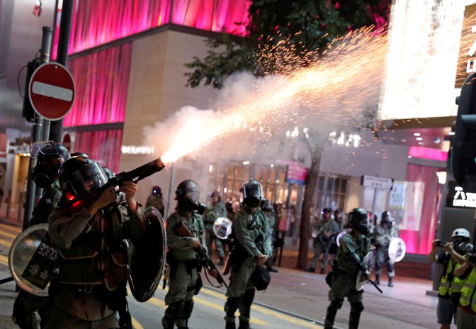 A Hong Kong police officer wearing a plastic protective mask fires a tear gas cannister.