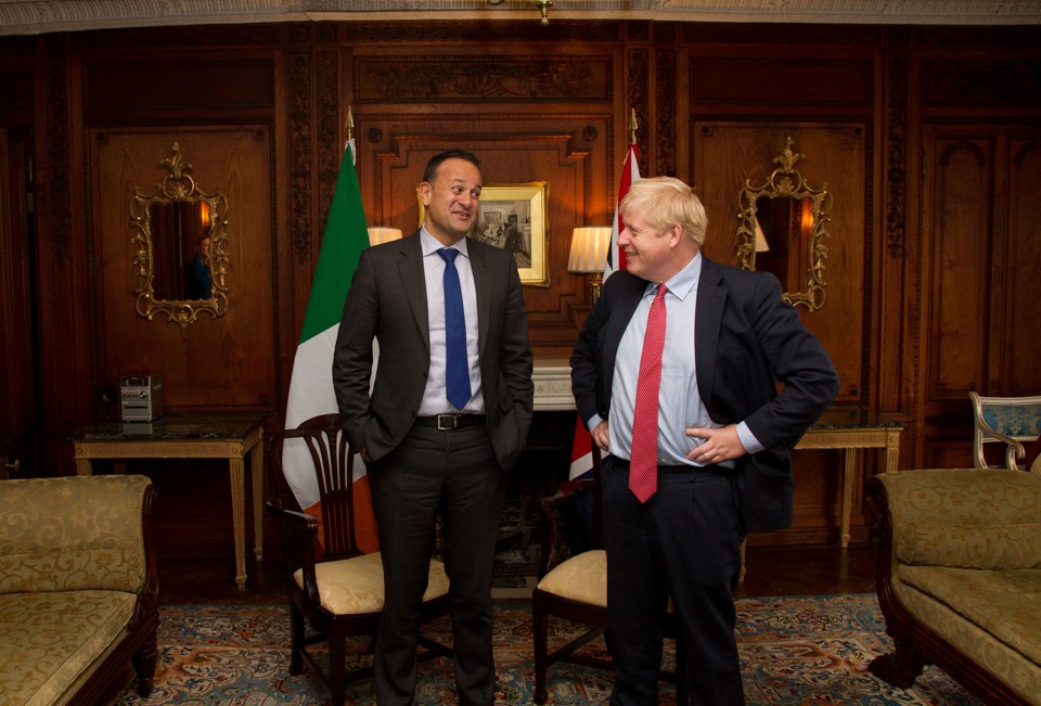 Boris Johnson and Leo Varadkar stand in front of chairs in a meeting room.