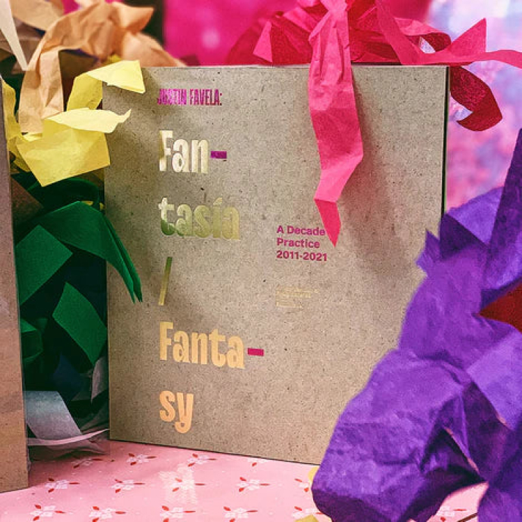 A brown book that has "Justin Favela: Fan-tasía / Fanta-sy" in gold and pink lettering on the front. 