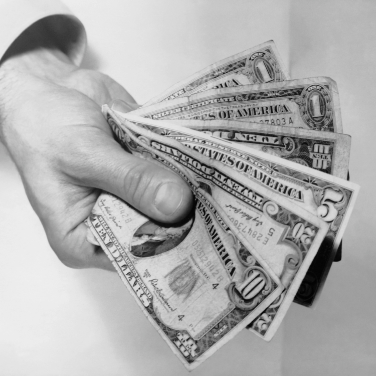 A black-and-white photo of someone holding out paper bills. 