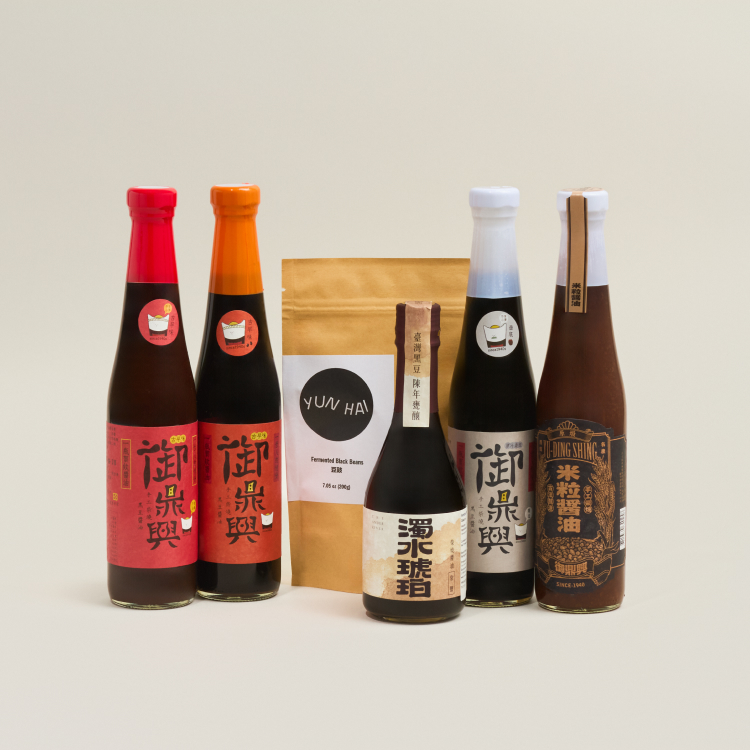 A display of five different soy sauces and a brown packet of fermented black beans. 