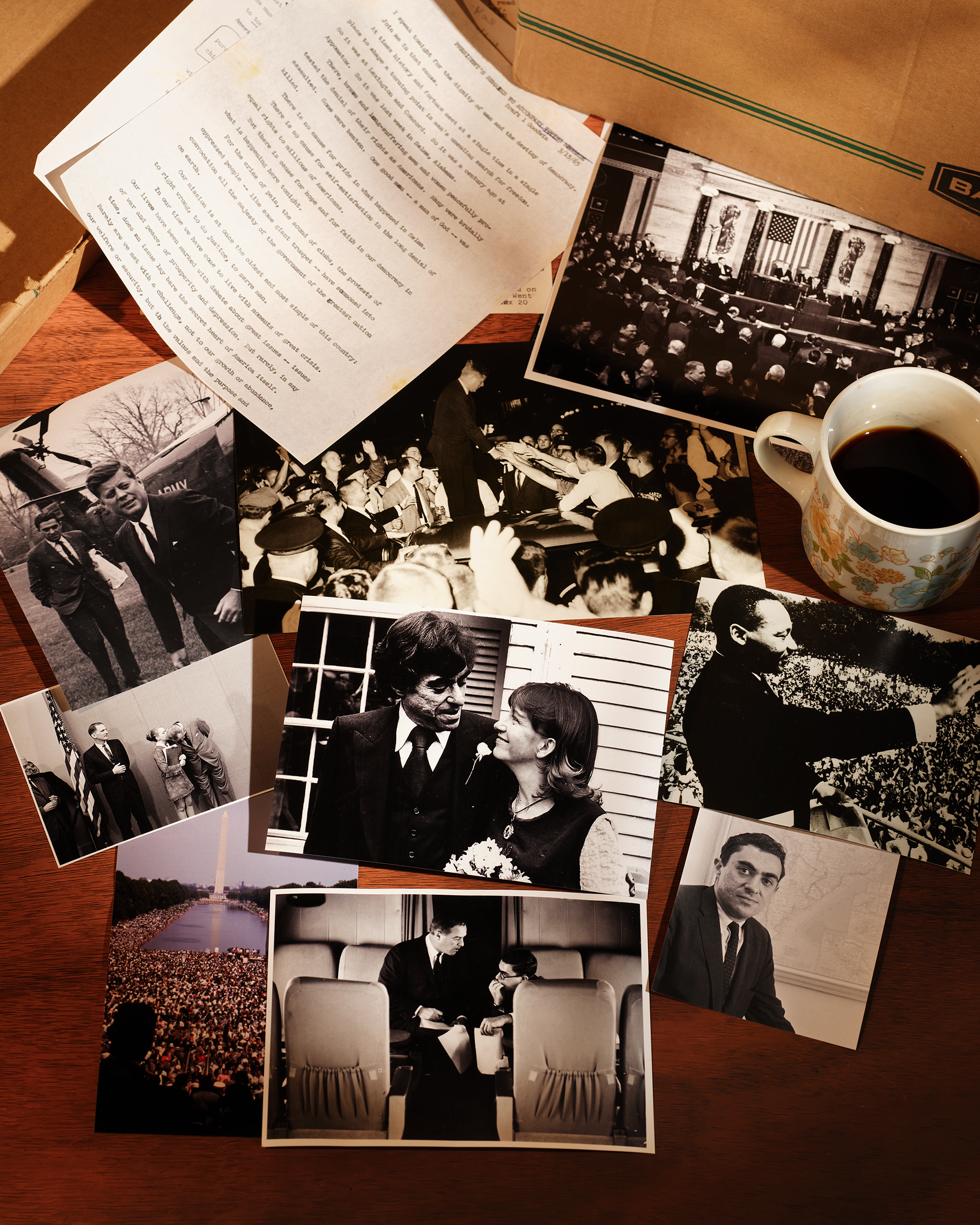 Multiple old pictures and documents next to a brown cardboard box and a cup of coffee