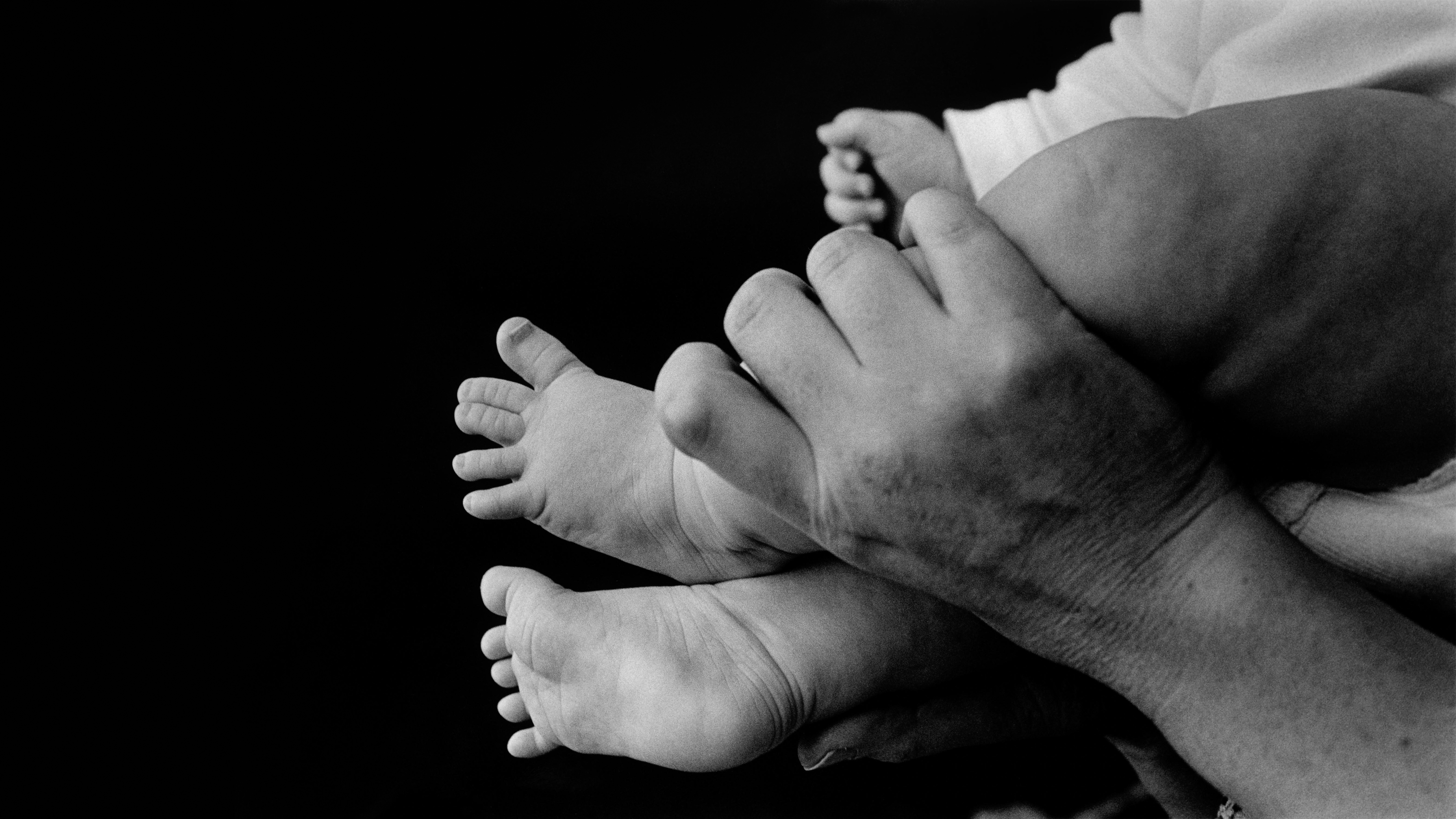 an adult's hand holds up a baby's feet, in greyscale