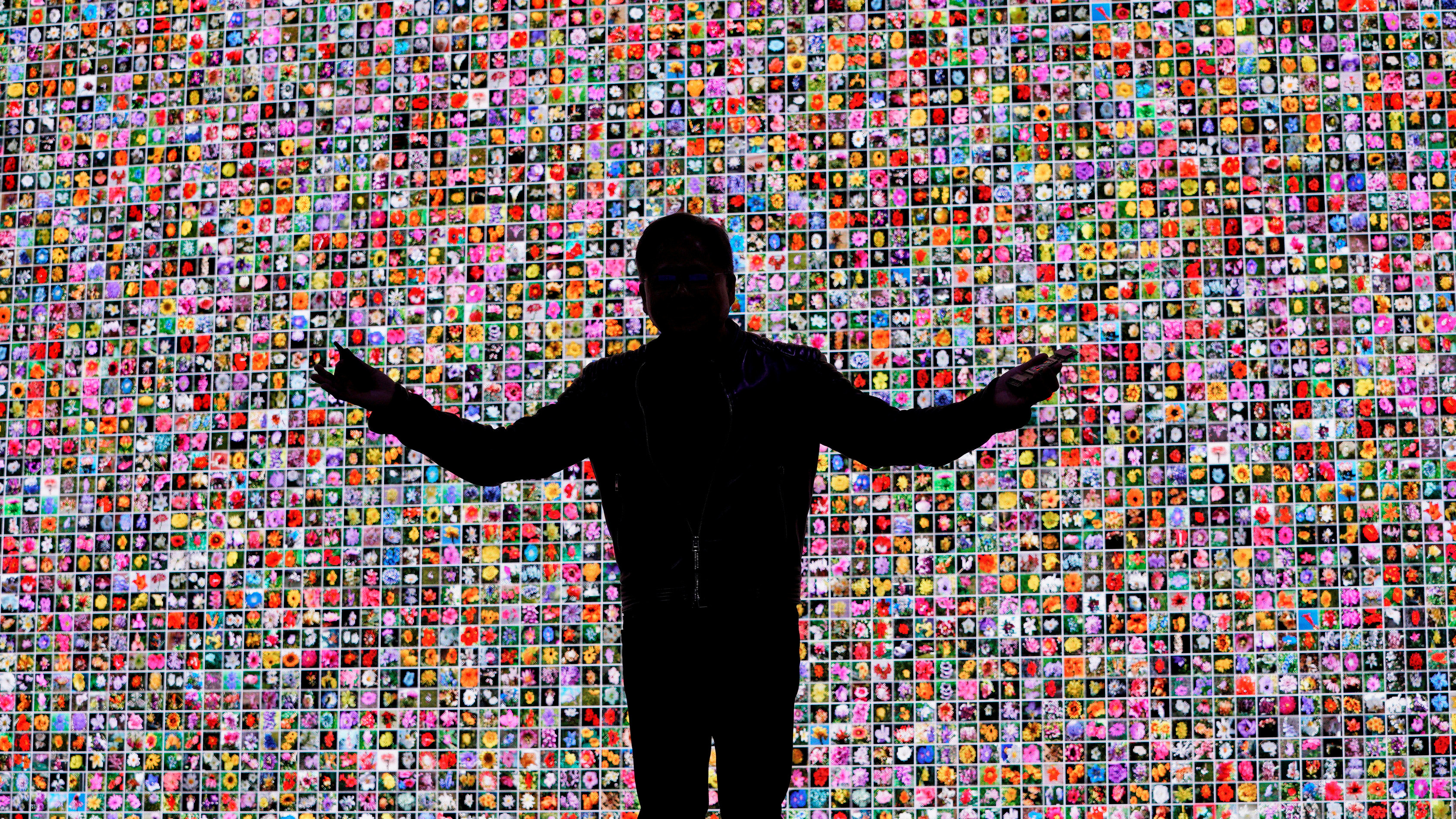 A photo of Jensen Huang in silhouette in front of a mosaic of small photos of flowers, delivering a keynote address at CES in 2018