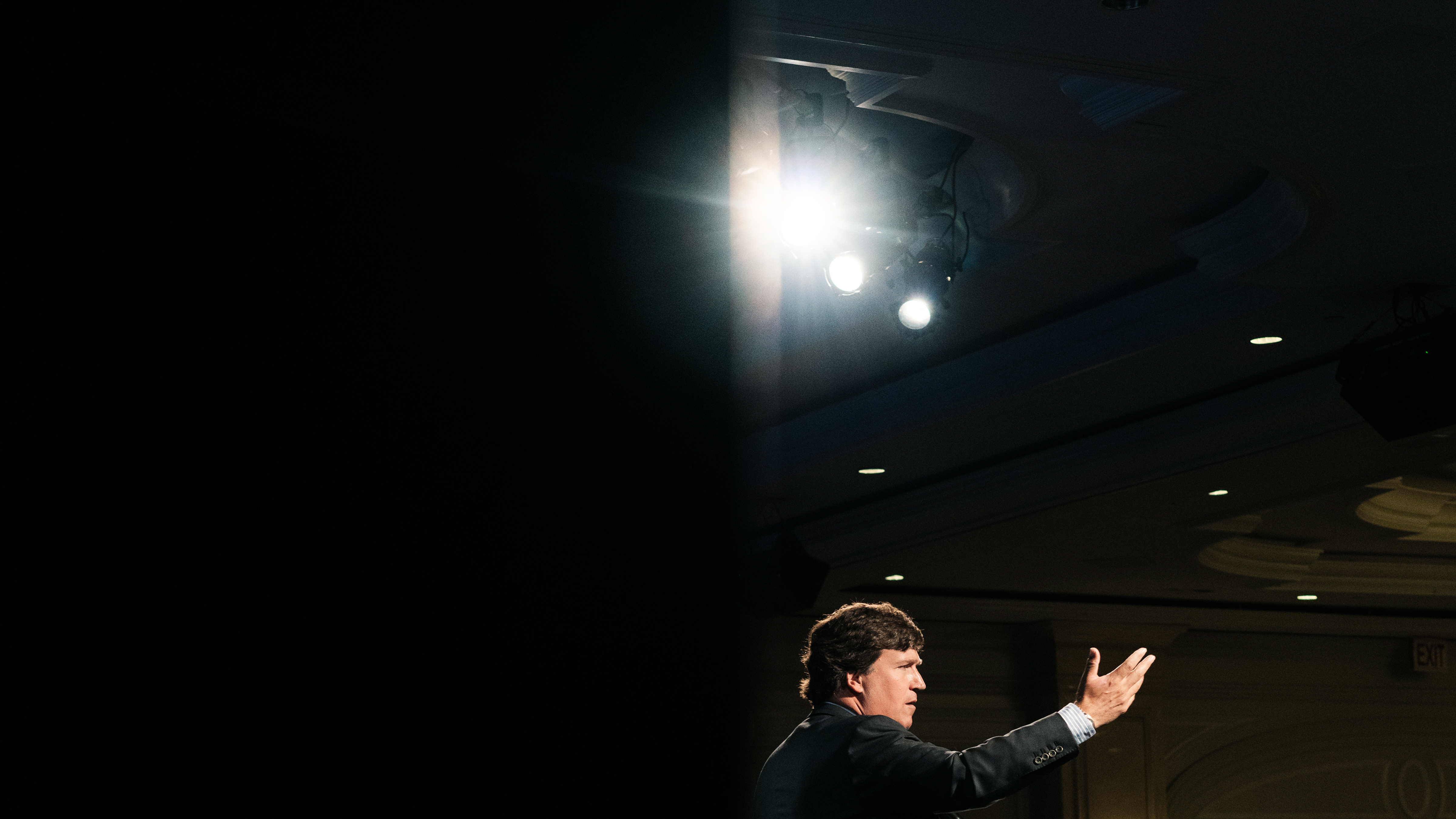 Tucker Carlson addresses an audience with a spotlight overhead.