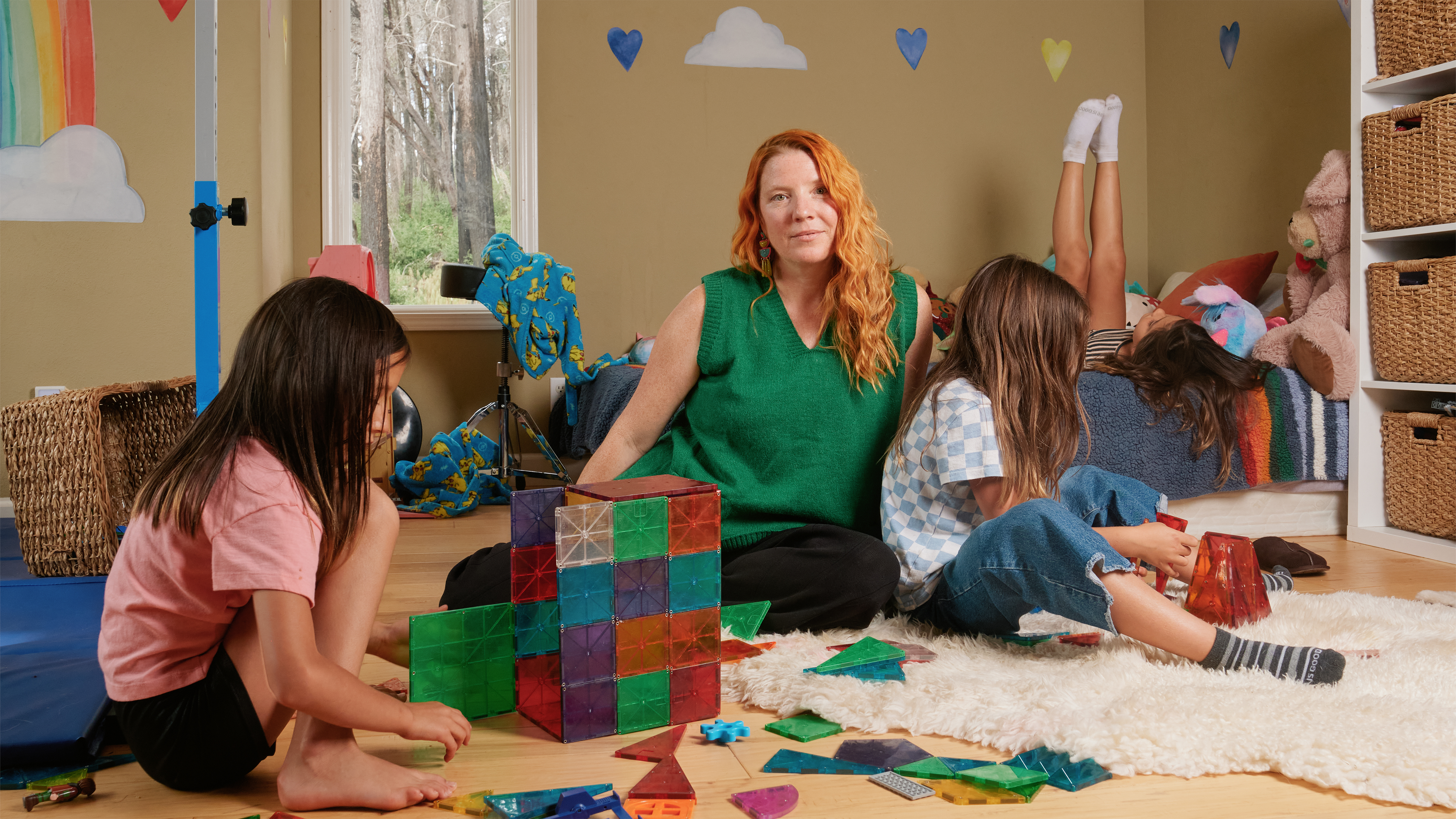 A woman sits on the floor of a bedroom while three children play by themselves.