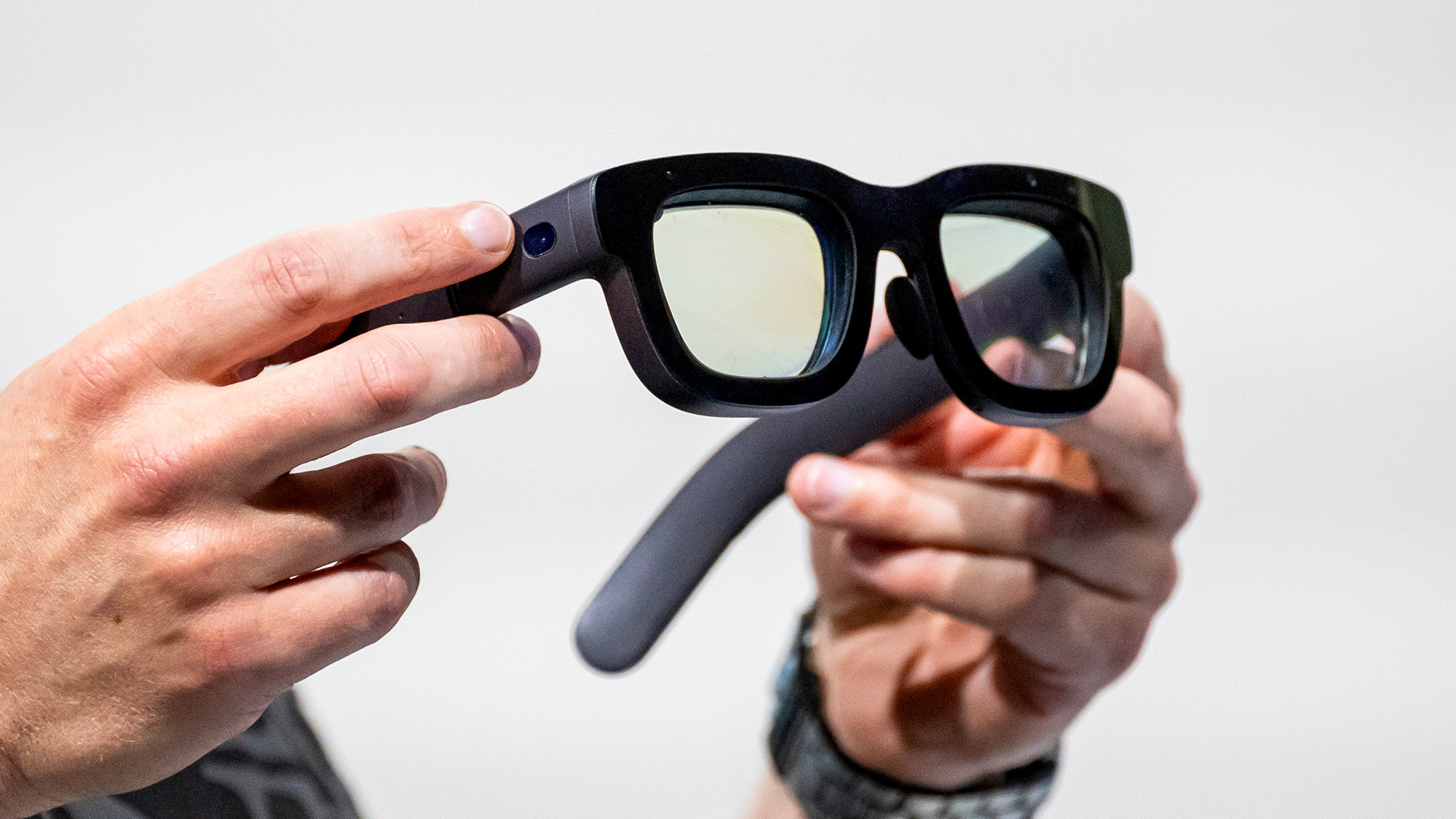 Una persona sosteniendo un par de gafas de realidad aumentada de gran tamaño y diseño grueso. Las gafas tienen un marco negro robusto y en las patillas se puede observar lo que parece ser una cámara integrada. Las lentes tienen un leve tinte, lo que sugiere que son parte de un dispositivo tecnológico avanzado, posiblemente prototipo, como las gafas Orion de Meta.