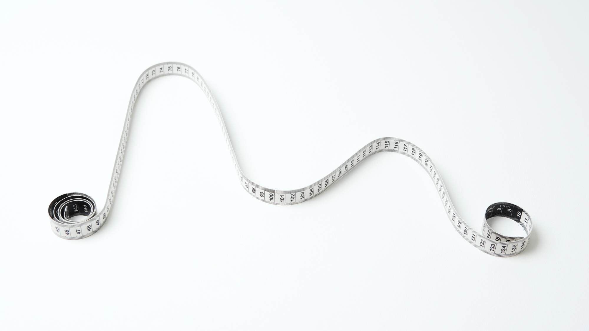 a white measuring tape curled into a graph-like curve with two peaks against a white background