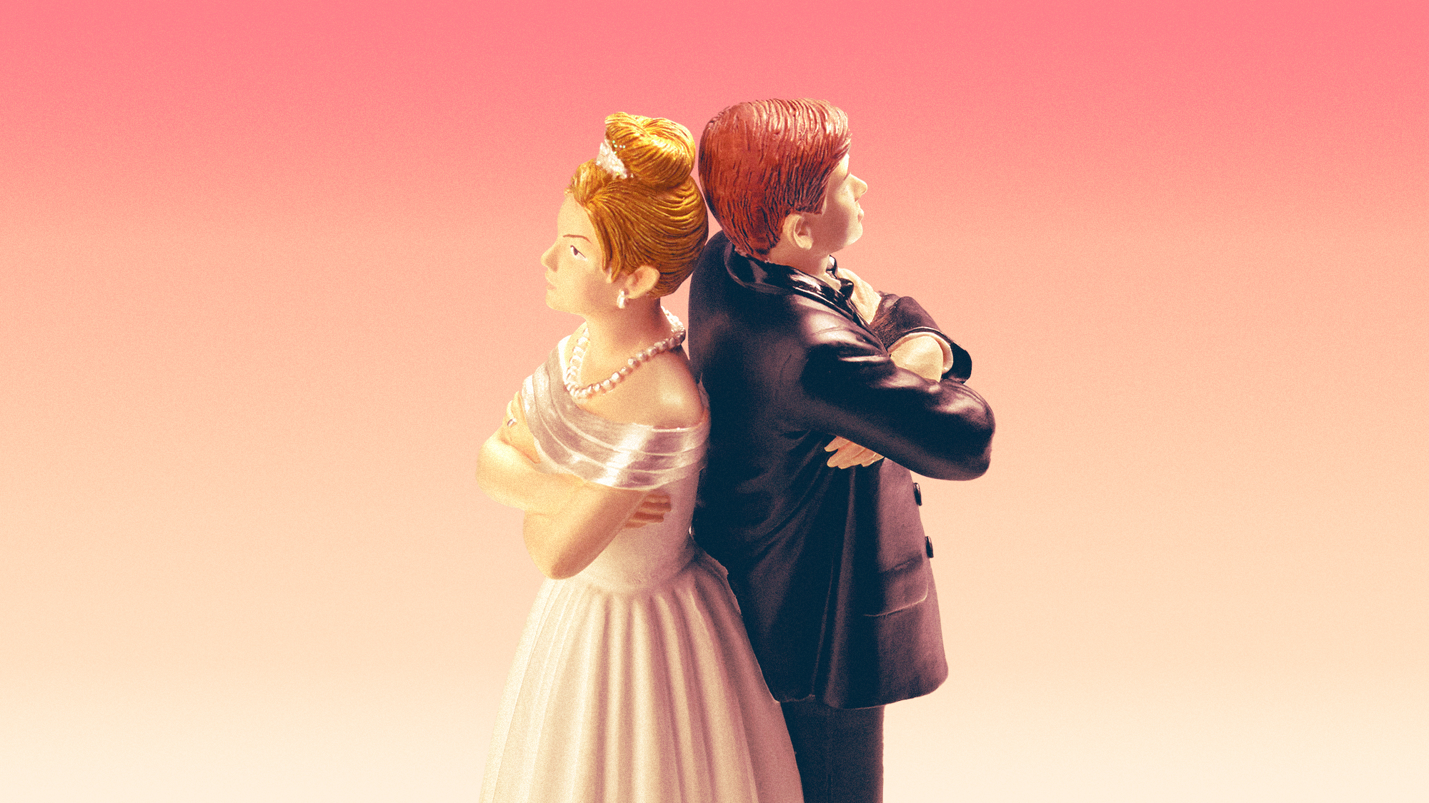 Wedding-cake bride and groom figurines standing back to back with their arms crossed