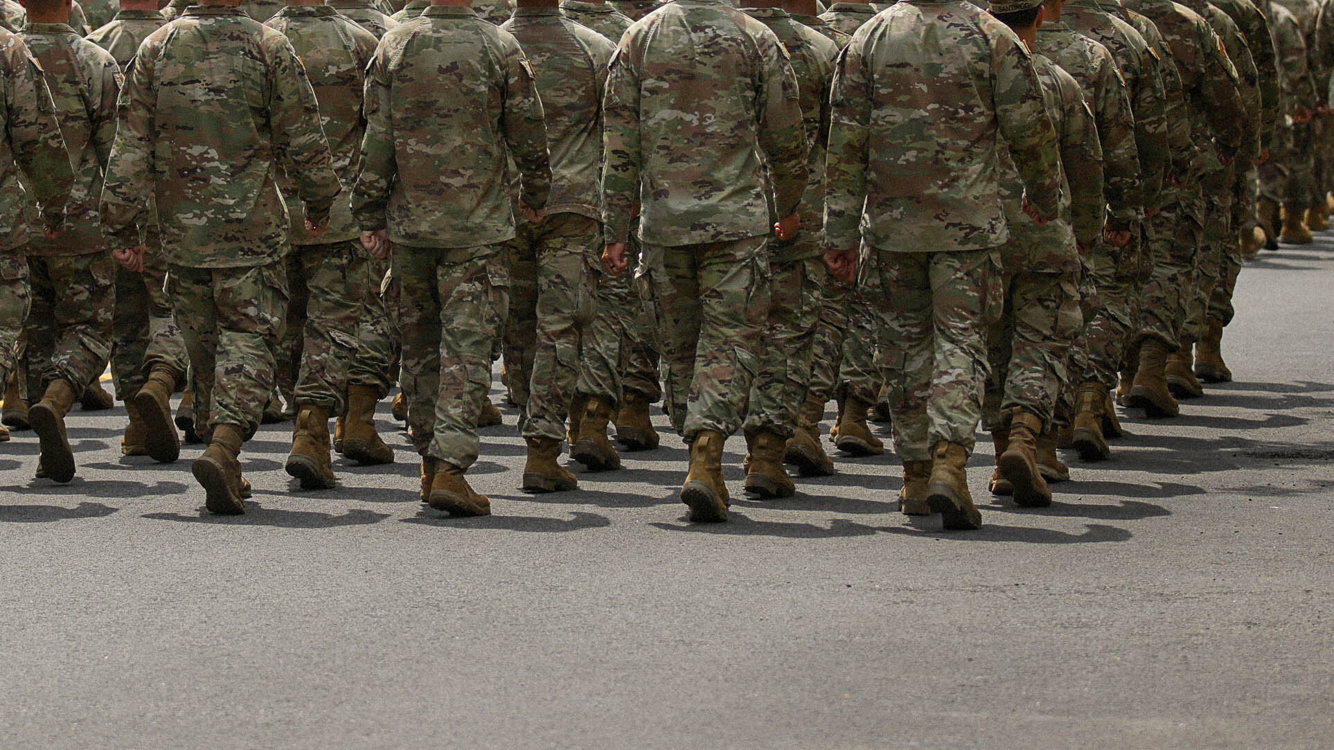 Members of the armed forces march forward, the back of their heads just barely out of frame