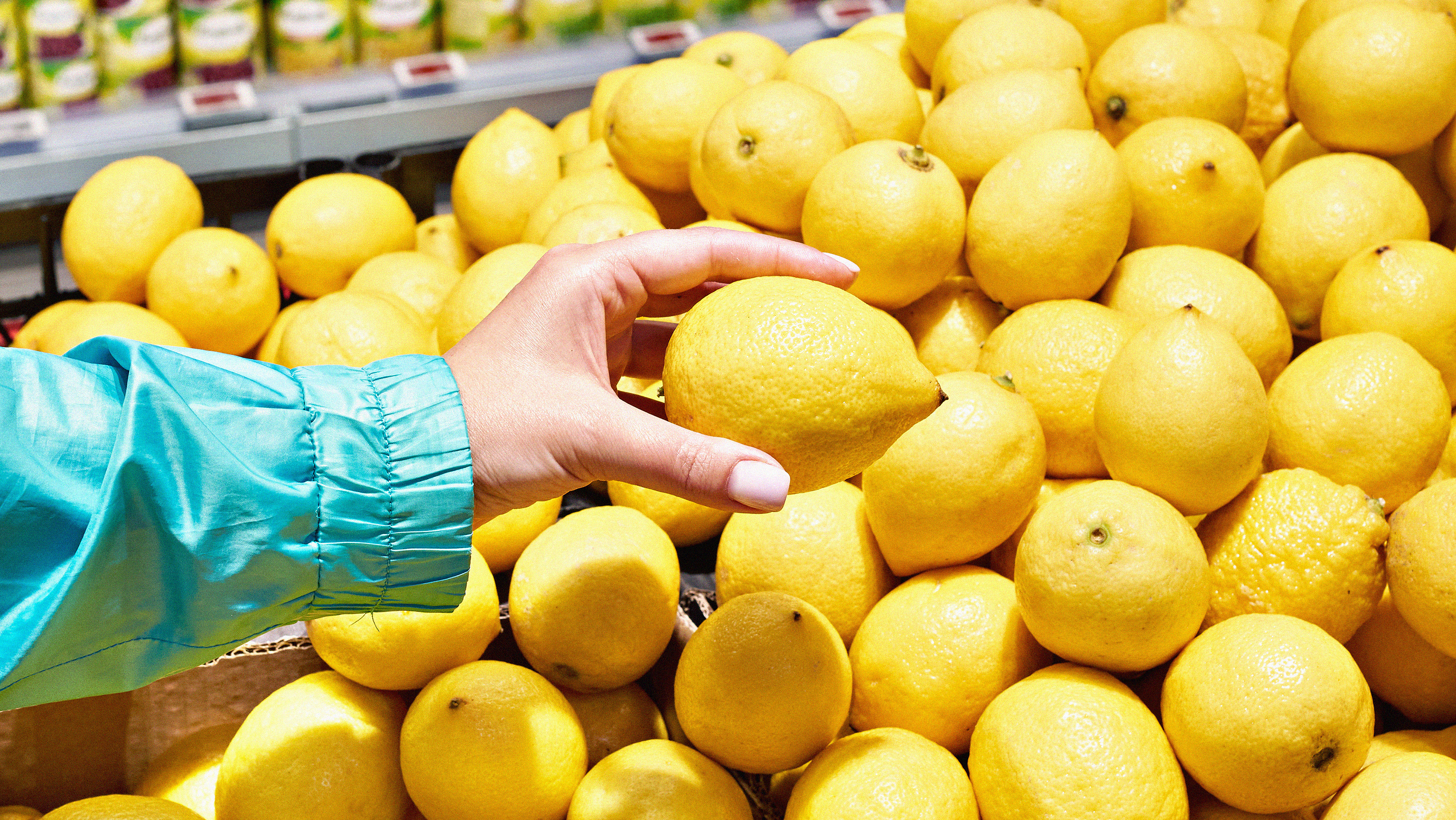 A color photo of someone picking up a lemon from a pile of them in a grocery store.