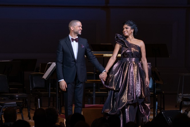 Jazz musicians Jason Moran and Alicia Hall Moran holding hands and smiling as they take their bows on a stage