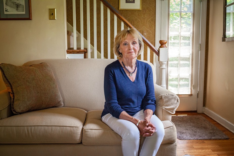 Photo of Helen McIlvaine sitting on a couch in front of stairs and a glass-paned door.