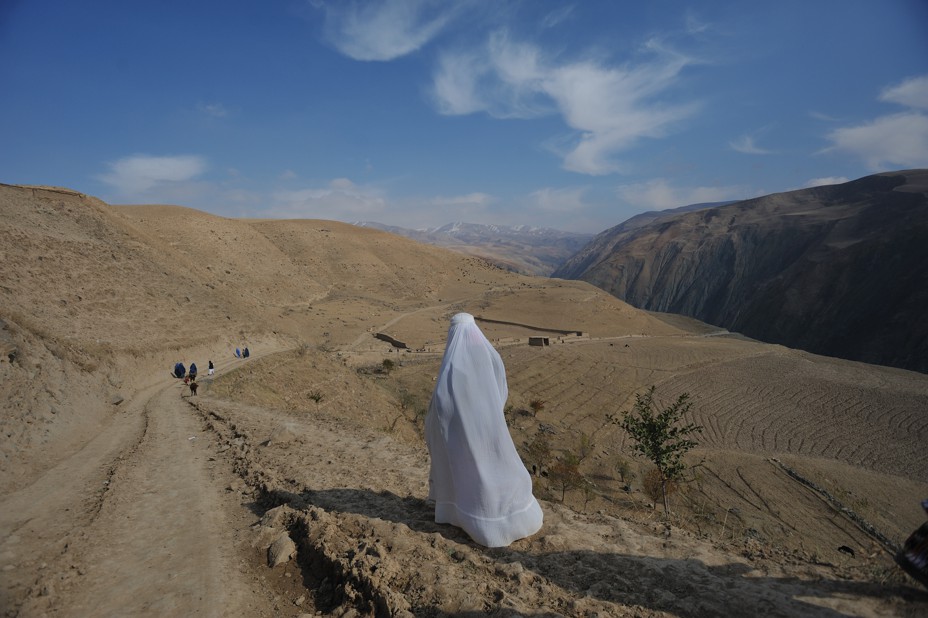 A woman walks along a rural road in a white Burqa