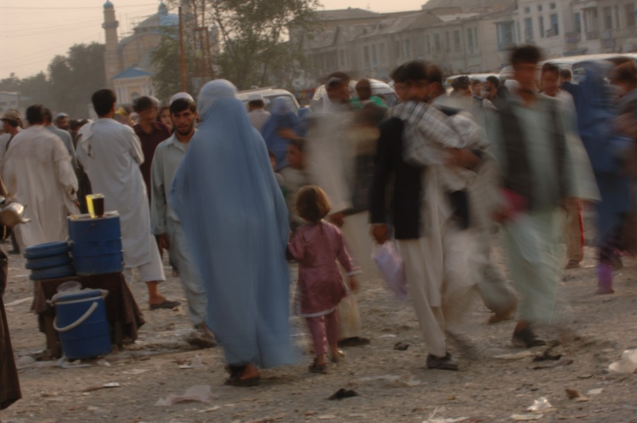 A woman in a burqa holds a small girls hand and moves through a crowded street