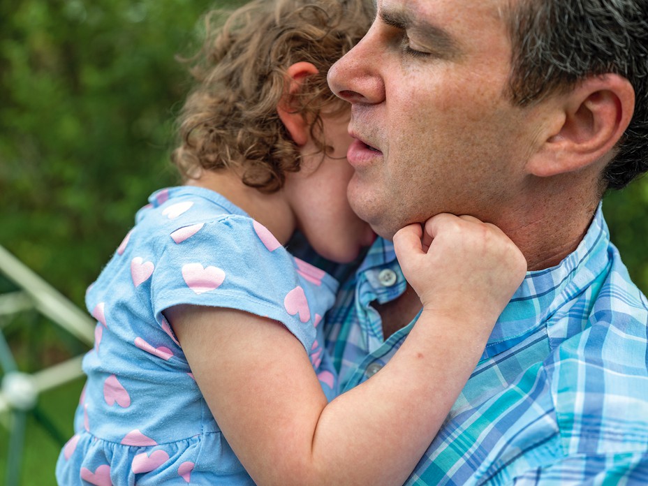 James, in profile with eyes closed, holds Livie, who has buried her face in his neck and touches his cheek with her hand