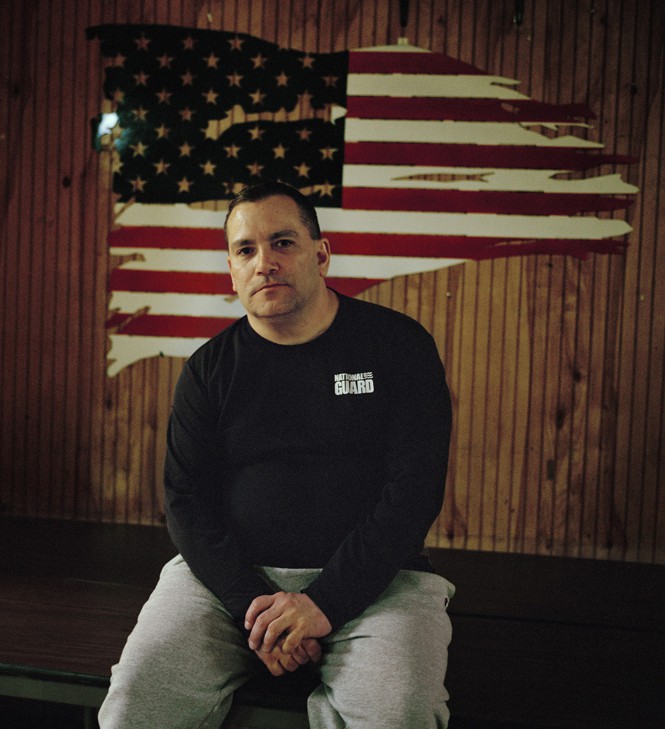 man sitting in front of a painted american flag