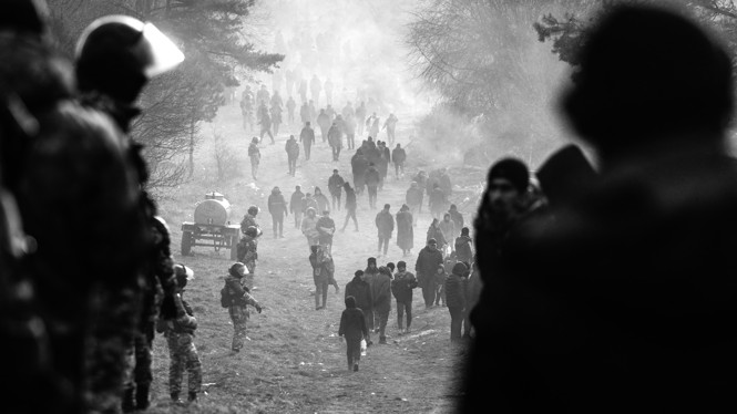 Migrants and soldiers are seen on a street.