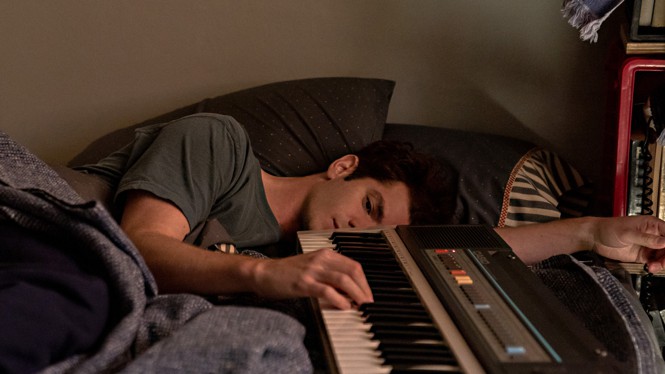 Andrew Garfield lying in bed and holding a keyboard in