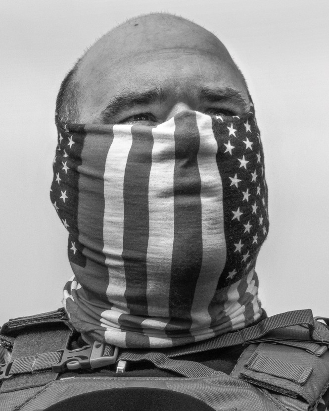 photo of balding man in tactical vest with an American flag face mask wrapped tightly around his head