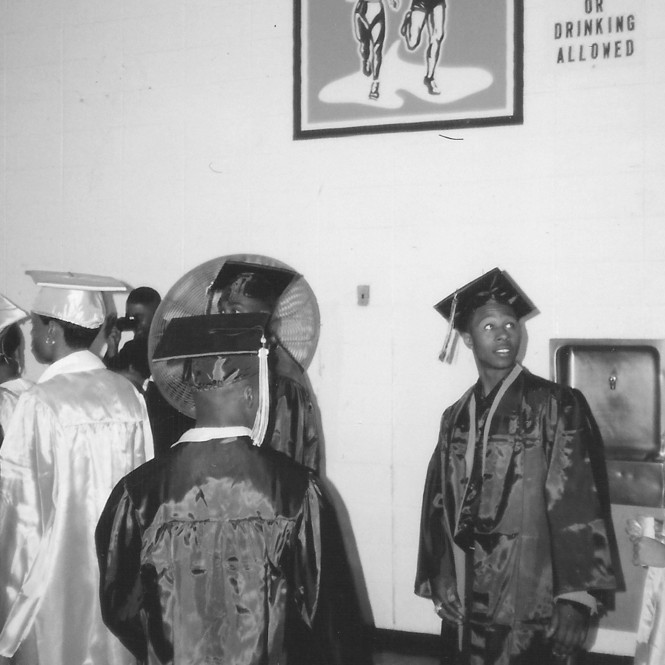 Jarrett in graduation robe in High School gym with other students
