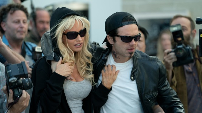 Pamela Anderson (Lily James) and Tommy Lee (Sebastian Stan) wearing sunglasses and walking through a crowd of photographers in "Pam & Tommy"