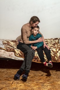 A mother hugs her son on a bed.