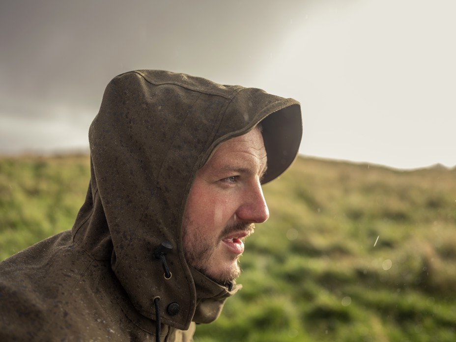 Profile of a man in a hooded raincoat in a Scottish landscape