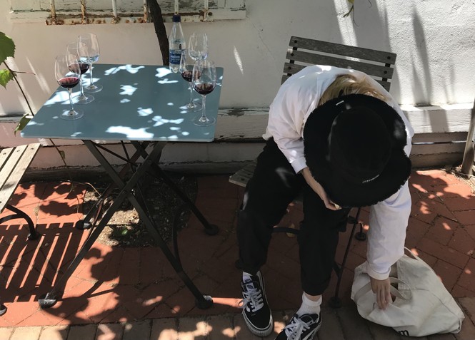 A table with six wine glasses on it, from a wine tasting. A woman pending over with a black hat covering her face.