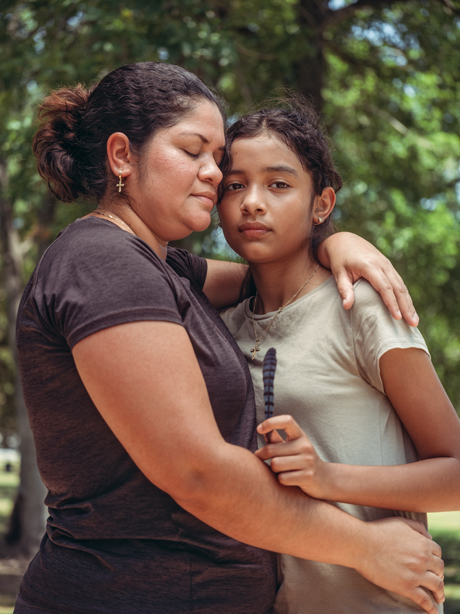 A photograph of Cindy Madrid with eyes closed and her arm around her daughter, Ximena, who looks at the camera and is holding a feather.