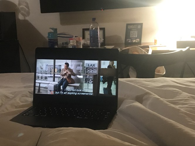 A laptop sitting on a hotel bed, playing the Japanese remake of Sideways.