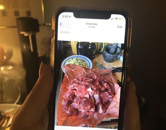 Kvindens hænder holder en telefon, telefonen viser et foto af rødt kød i tern.
