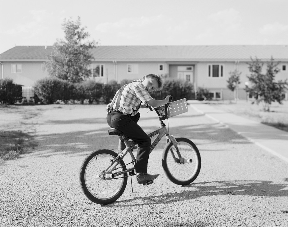 Black-and-white photo of boy riding bike in front of building
