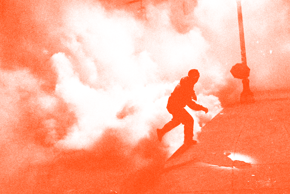 photo of masked person running on street in cloud of tear gas