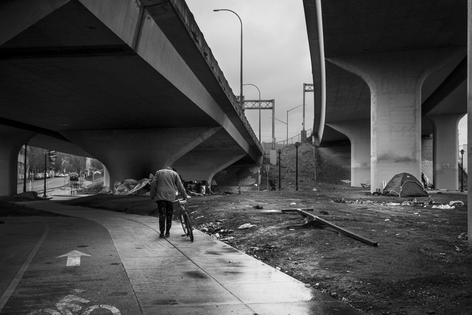 a person walks a bike under an overpass near tents