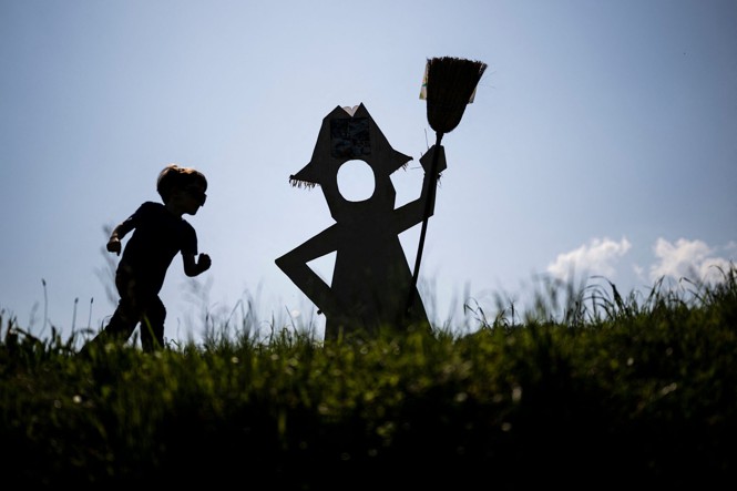 A child runs near a scarecrow displayed at the annual Scarecrows Fair in the Italian village of Castellar, near Cuneo, on May 22, 2023. During the fair, people exhibit—in gardens, courtyards, fields, or streets—scarecrows they have made. 