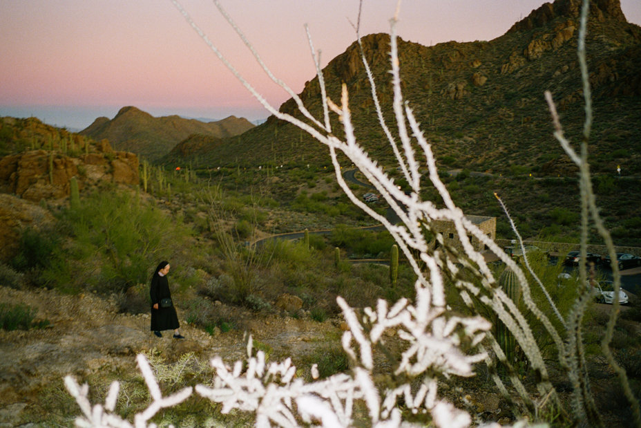 Photo at dawn or dusk with nun walking on a trail in the distance near desert mountains