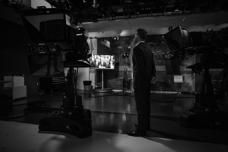 a tv studio where a man looks at a screen with people talking
